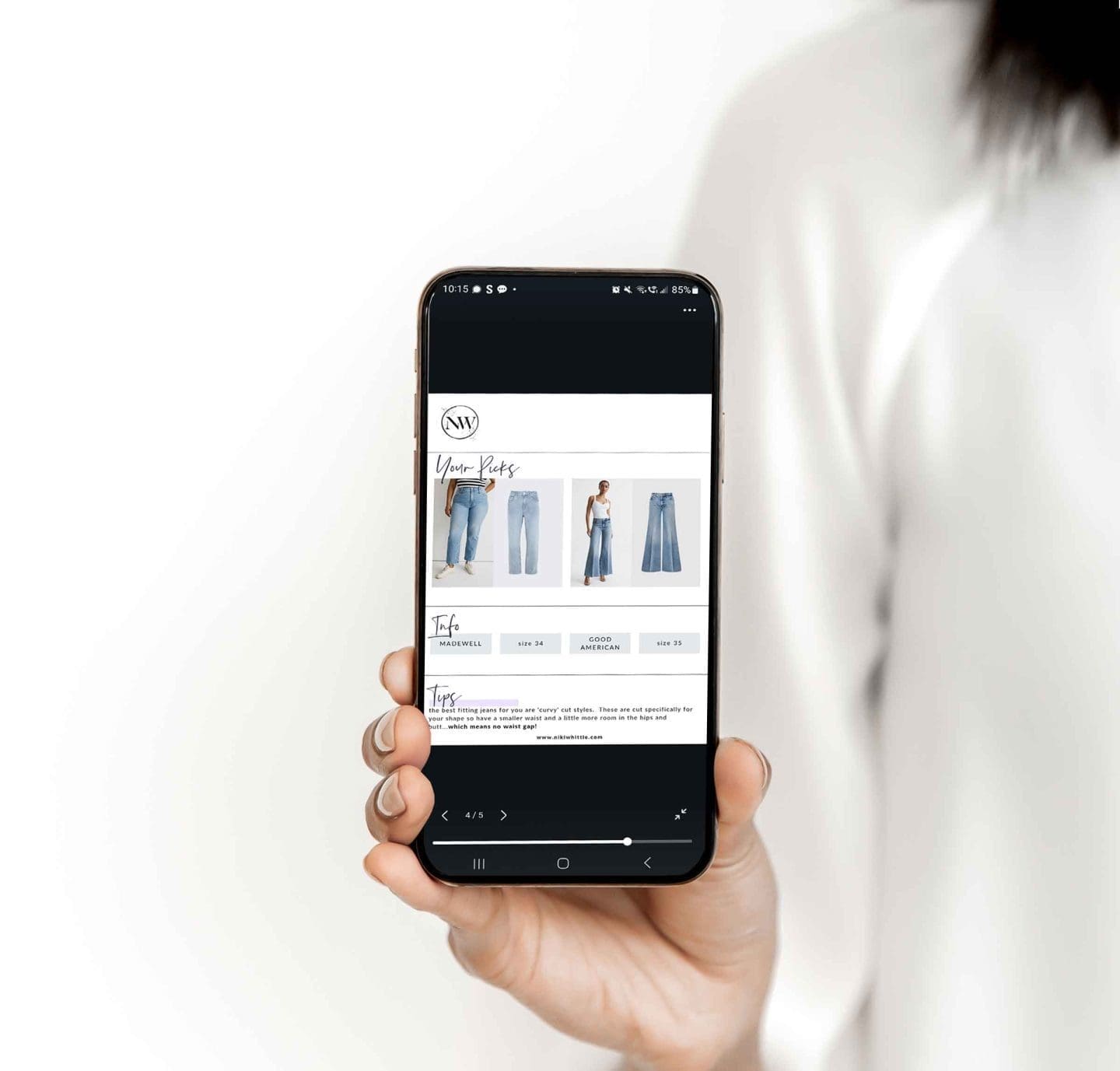 An image of a women holding a mobile phone with an image of an online shopping look book on the screen